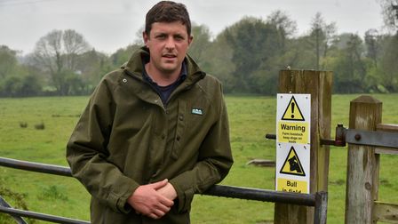 Cattle farmer Tom Seaman with signs warning walkers of livestock dangers on grazing land at Swardeston